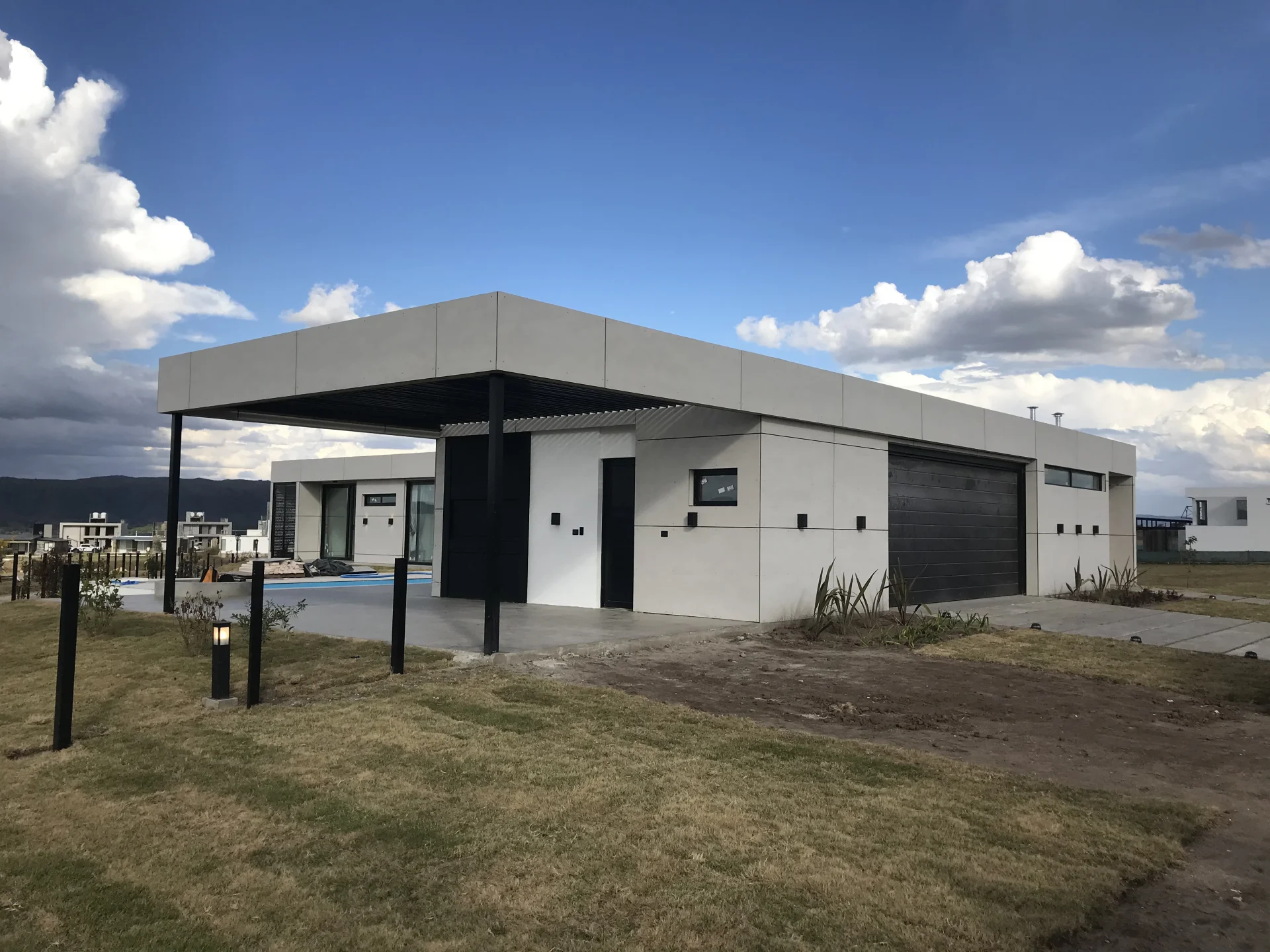 Foto de una casa en puerto del Águila construída con el sistema de Steel Framing por Vértice Construcciones en la que se observa la fachada de la casa revestida con doble placa marca Equitone y la puerta principal y el garage, desde el ángulo izquierdo de la casa