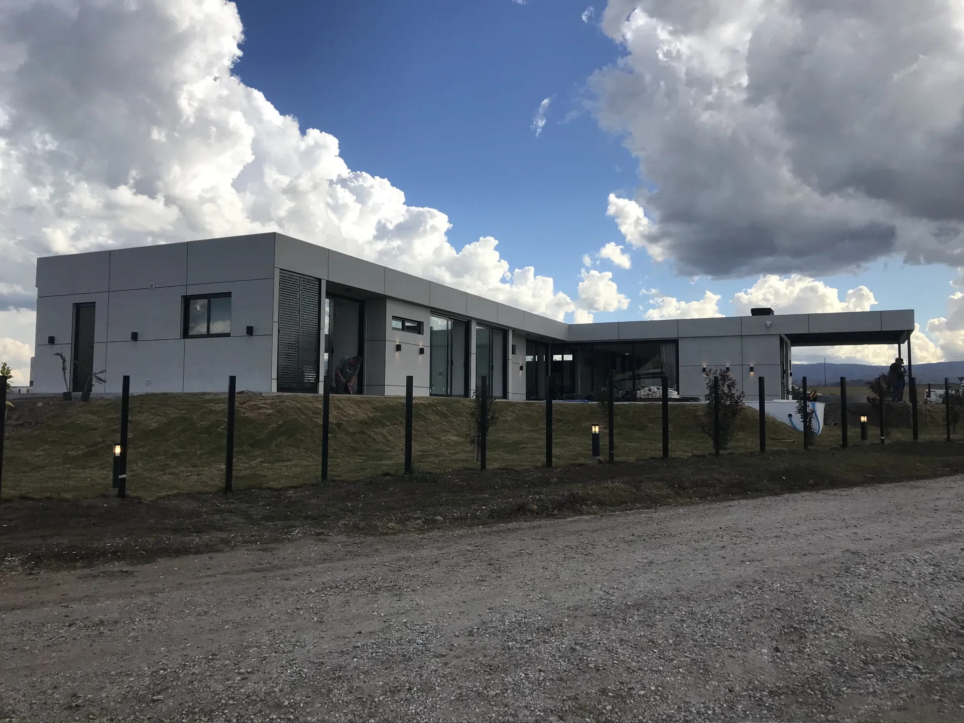 Foto de una casa en puerto del Águila construída con el sistema de Steel Framing por Vértice Construcciones en la que se observa en primer plano la calle y más atrás el patio trasero y una galería en forma de L de la casa revestida con doble placa marca Equitone