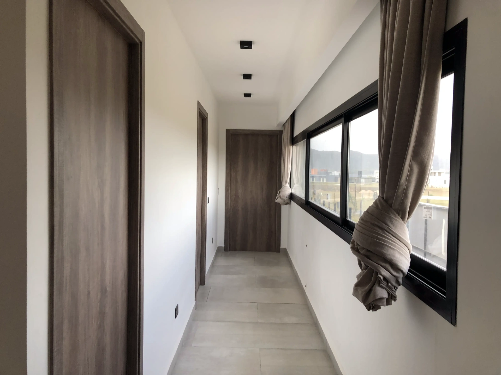 Foto de una casa en puerto del Águila construída con el sistema de Steel Framing por Vértice Construcciones en la que se observa un pasillo interior con dos puertas a la izquierda, una tercer puerta al fondo, y un ventanal a la derecha