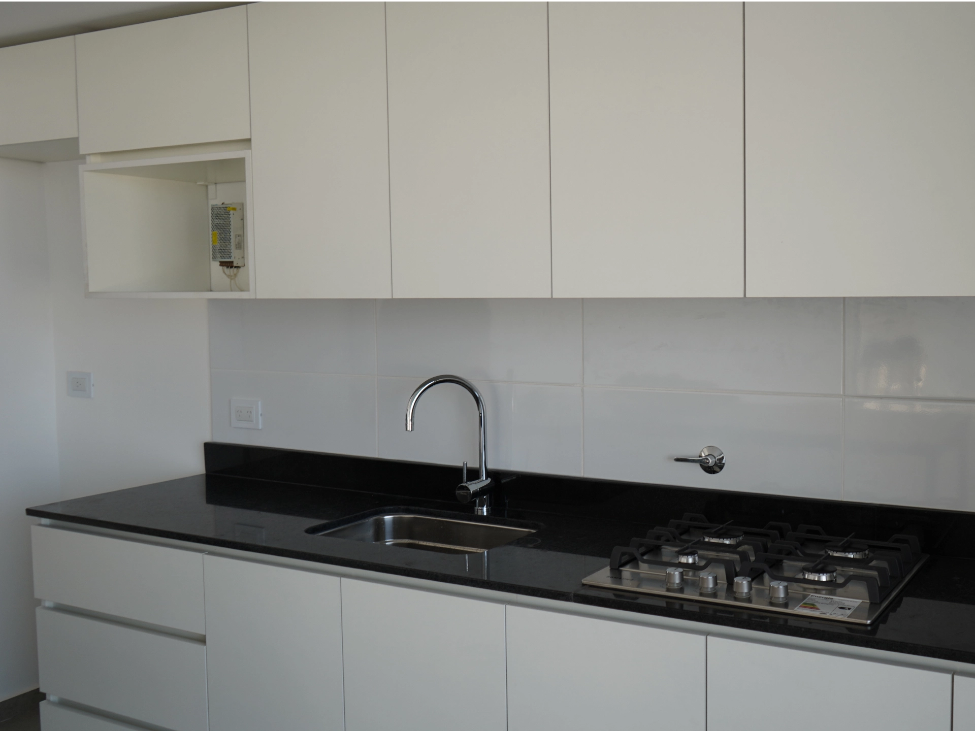 Foto de una casa en puerto del Águila construída con el sistema de Steel Framing por Vértice Construcciones en la que se observa en primer plano la cocina con muebles blancos y una mesada de mármol negro que tiene anafe y bacha para lavar los platos