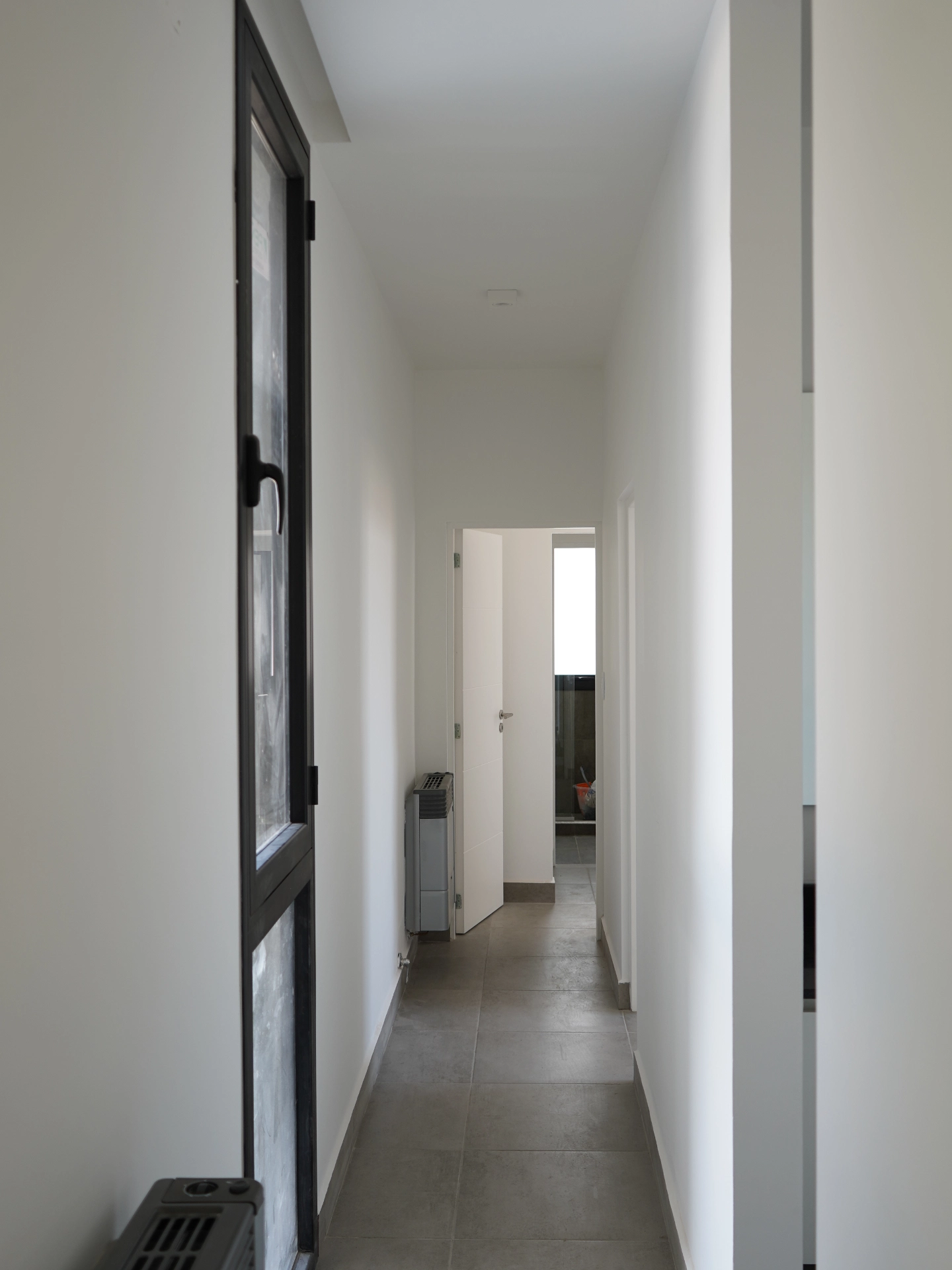Foto de una casa en puerto del Águila construída con el sistema de Steel Framing por Vértice Construcciones en la que se observa un pasillo interior con habitaciones del lado derecho y al fondo, y una pared con una ventana vertical a la izquierda