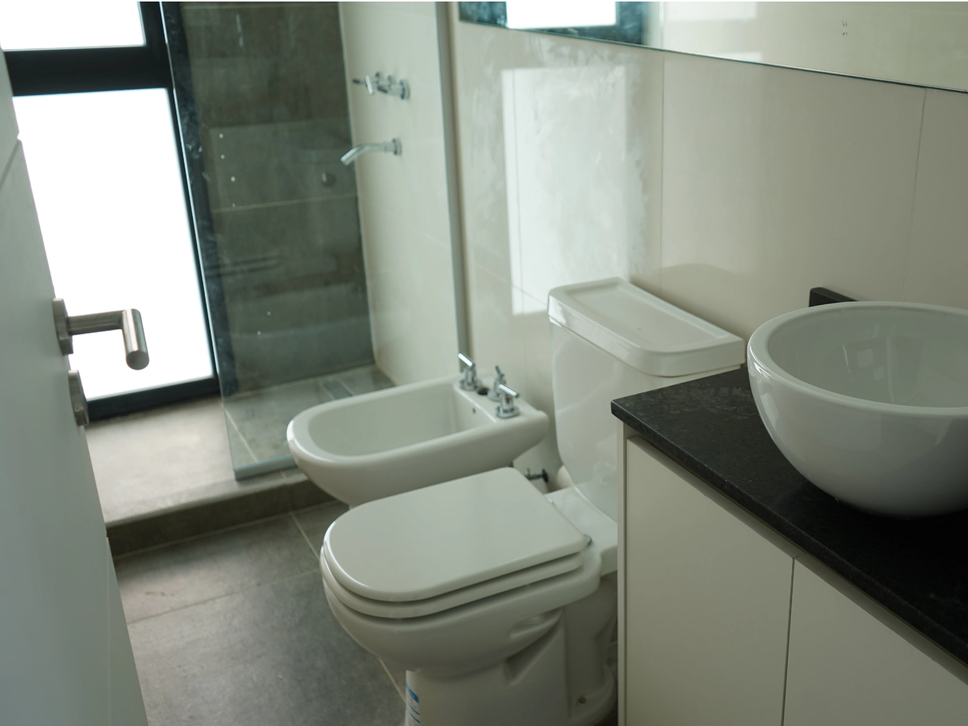 Foto de una casa en puerto del Águila construída con el sistema de Steel Framing por Vértice Construcciones en la que se observa un baño con mueble con bacha, inodoro, bidet y ducha con mampara de vidrio