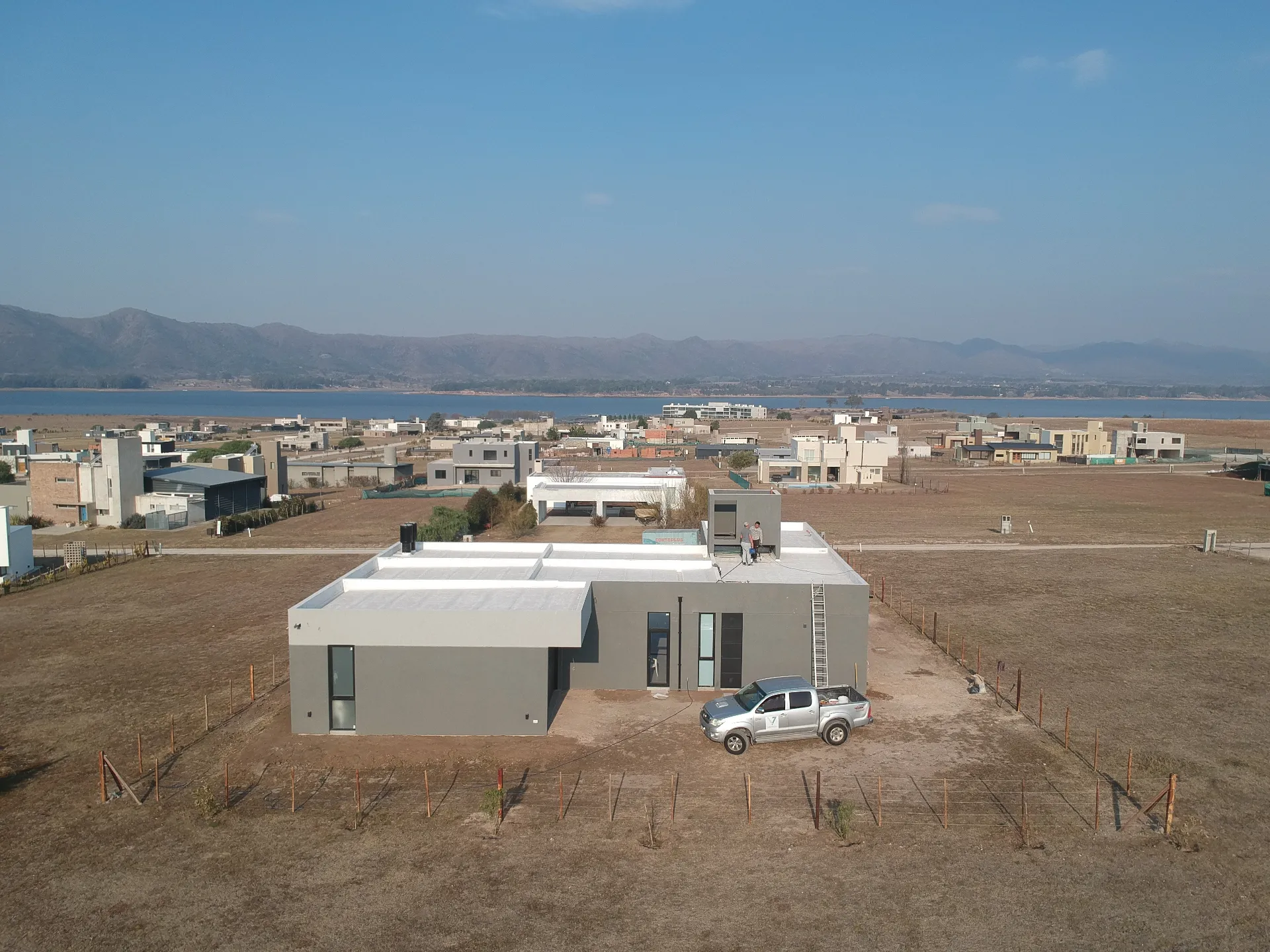 Foto de una casa en puerto del Águila construída con el sistema de Steel Framing por Vértice Construcciones en la que se observa la fachada trasera de la casa revestida con el sistema EIF's dándole una terminación final con revestimiento texturado. Al fondo se encuentra el lago en medio de un valle