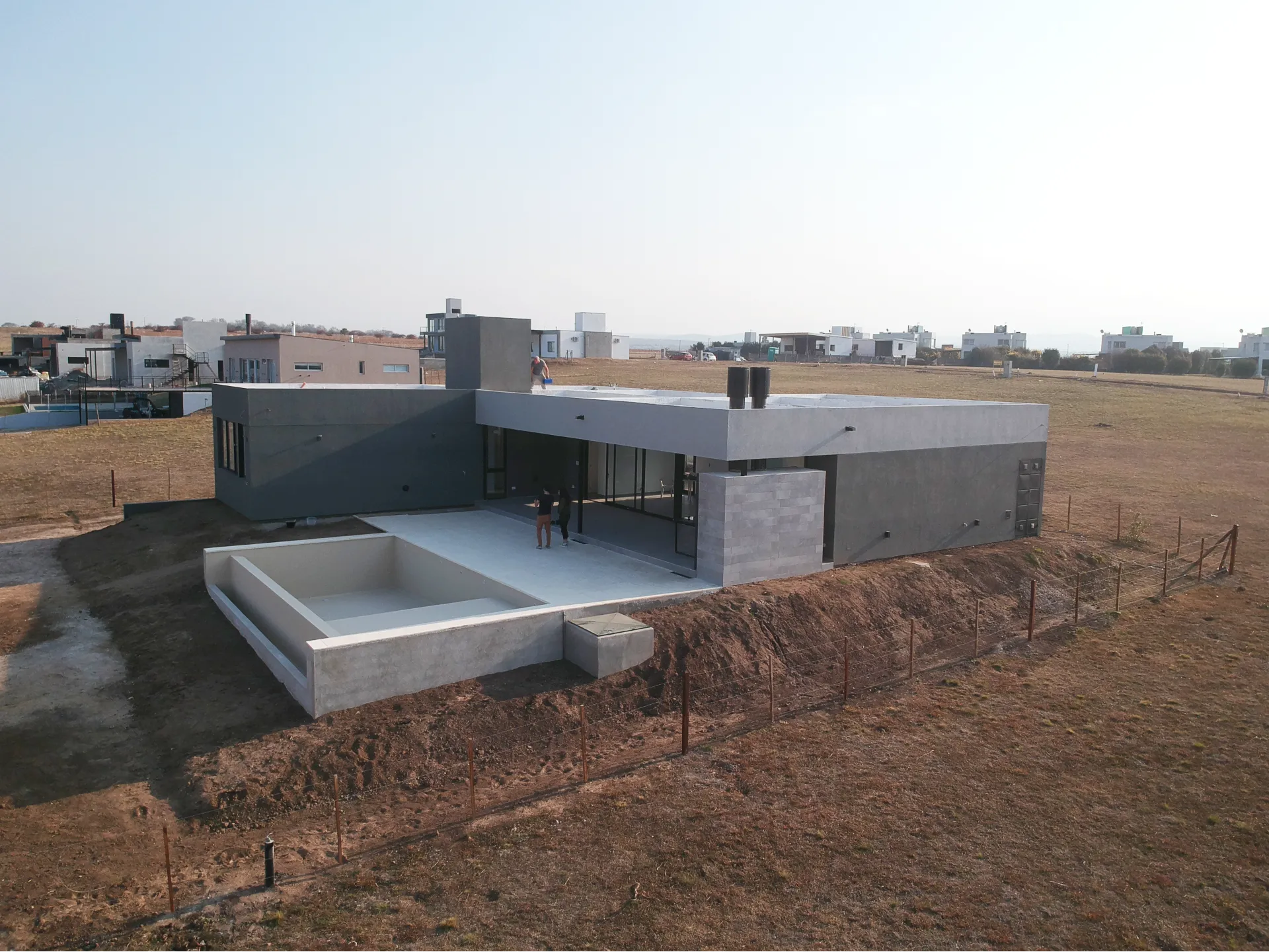 Foto de una casa en puerto del Águila construída con el sistema de Steel Framing por Vértice Construcciones en la que se observa la fachada lateral de la casa revestida con el sistema EIF's dándole una terminación final con revestimiento texturado, en la que se encuentra una galería con dos chimeneas que pertenecen a un asador y una pileta