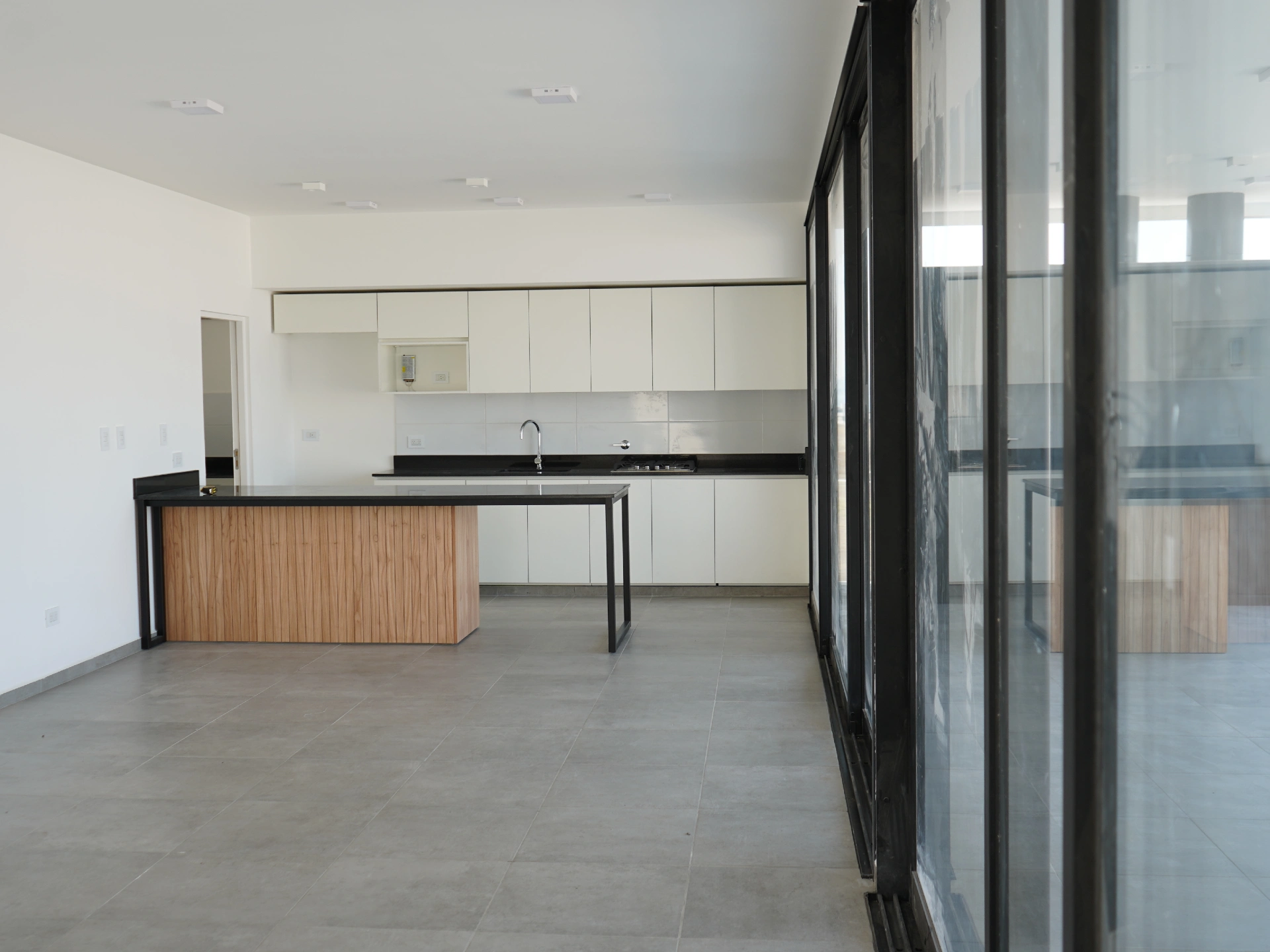 Foto de una casa en puerto del Águila construída con el sistema de Steel Framing por Vértice Construcciones en la que se observa la cocina con muebles blancos y una mesada de mármol negro idéntica a la que tiene la mesada en forma de isla revestida con madera