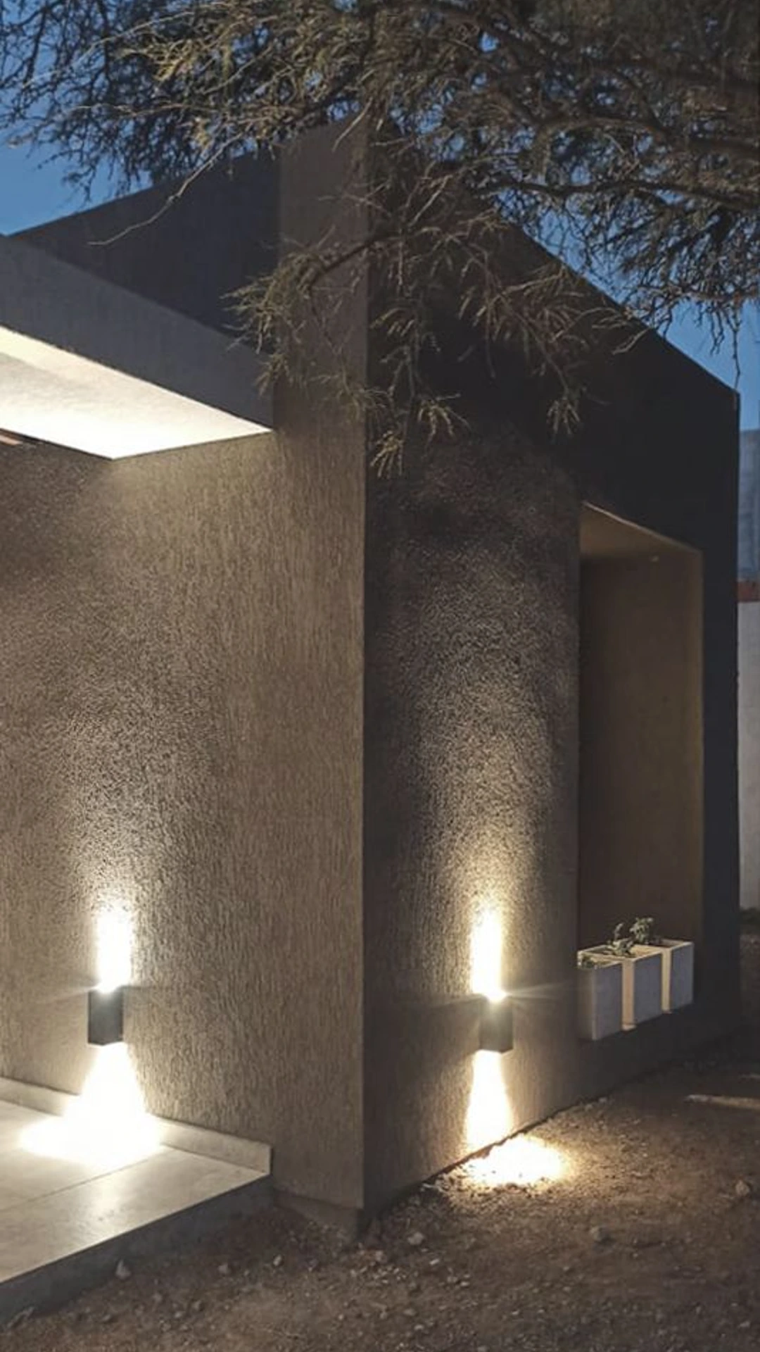 Foto de una casa en 7 Soles construída con el sistema de Steel Framing por Vértice Construcciones en la que se observa en primer plano un ángulo de la fachada de la casa revestida con el sistema EIF´s, iluminada con luces prendidas ya que es de noche