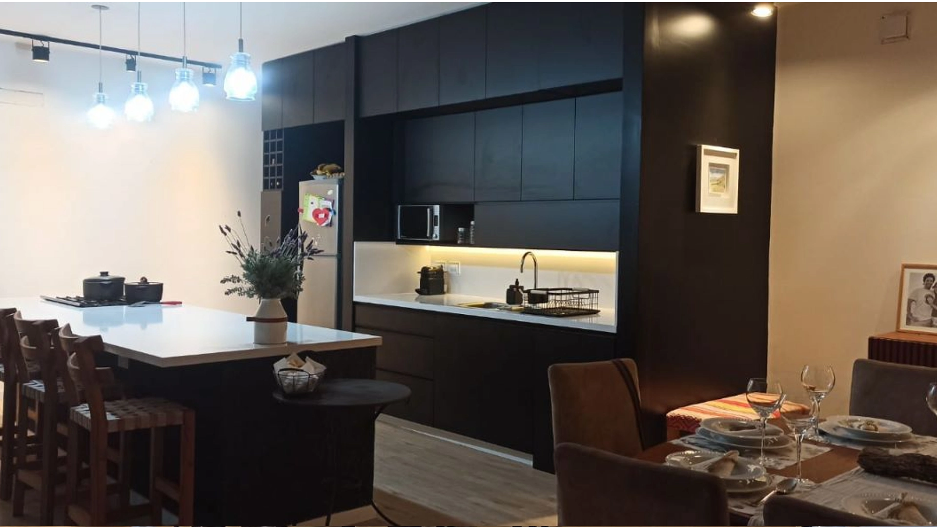 Foto de una casa en 7 Soles construída con el sistema de Steel Framing por Vértice Construcciones en la que se observa la cocina con muebles de madera marrón oscuro y una isla al centro con una mesada alta tipo barra y sillas altas y a un costado hay una mesa puesta y sillas