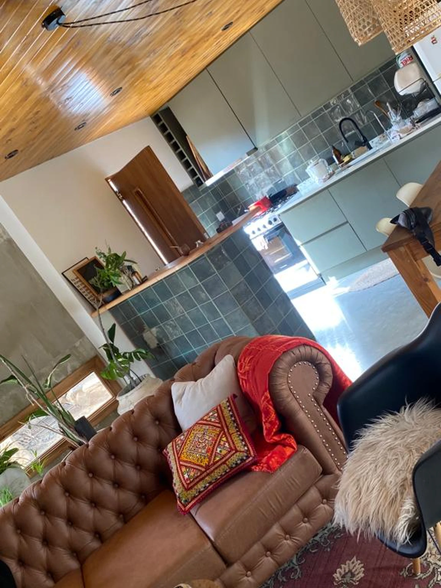 Foto de una casa en Bialet Massé construída con el sistema de Steel Framing por Vértice Construcciones en la que se observa una sala de estar interior con un sillón símil cuero color marrón, más atrás una barra revestida de azulejos de un tono azulado y tapa de madera y una cocina con paredes también revestidas de azulejos de un tono azulado y muebles de cocina haciendo juego de un tono azulado; el piso es de hormigón alisado color gris plomo, el techo de madera
