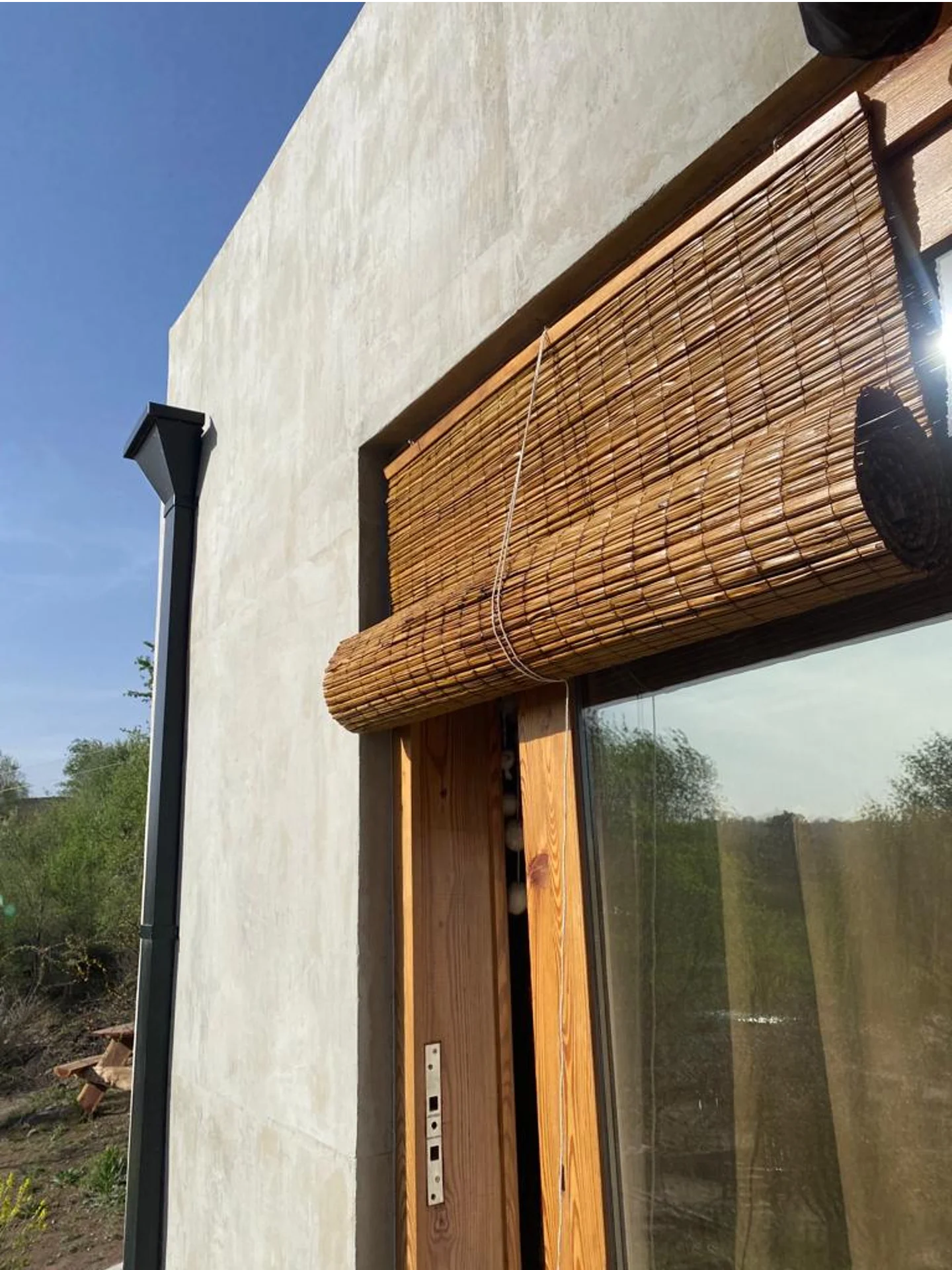 Foto de una casa en Bialet Massé construída con el sistema de Steel Framing por Vértice Construcciones en la que se observa en primer plano parte de la fachada de la casa con un acabado símil hormigón visto y una puerta-ventana con aberturas de madera