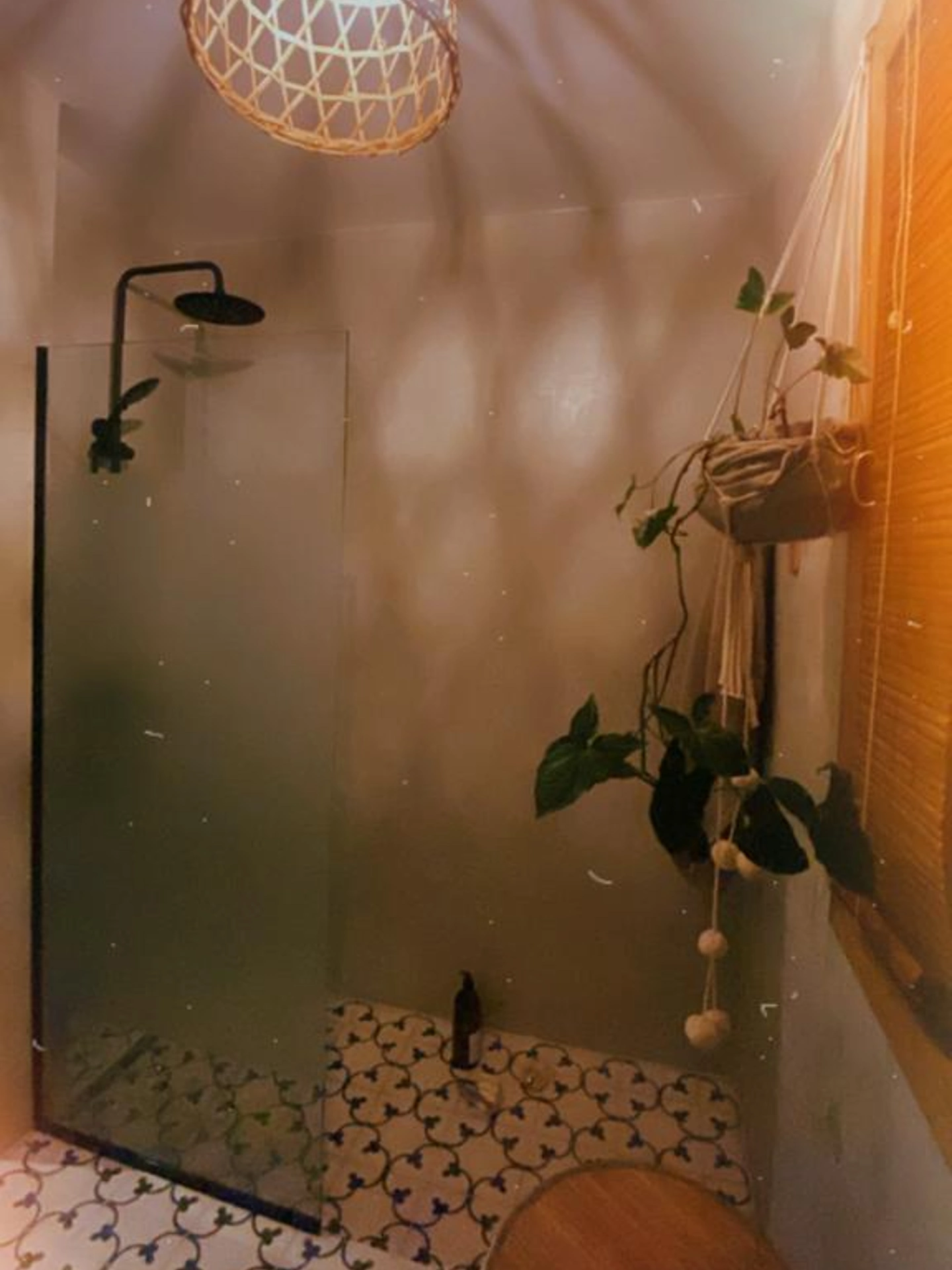 Foto de una casa en Bialet Massé construída con el sistema de Steel Framing por Vértice Construcciones en la que se observa un baño con una ducha y una mampara de vidrio; el piso es de azulejos blancos ornamentados con azul y las paredes y techo son de hormigón alisado color gris plomo