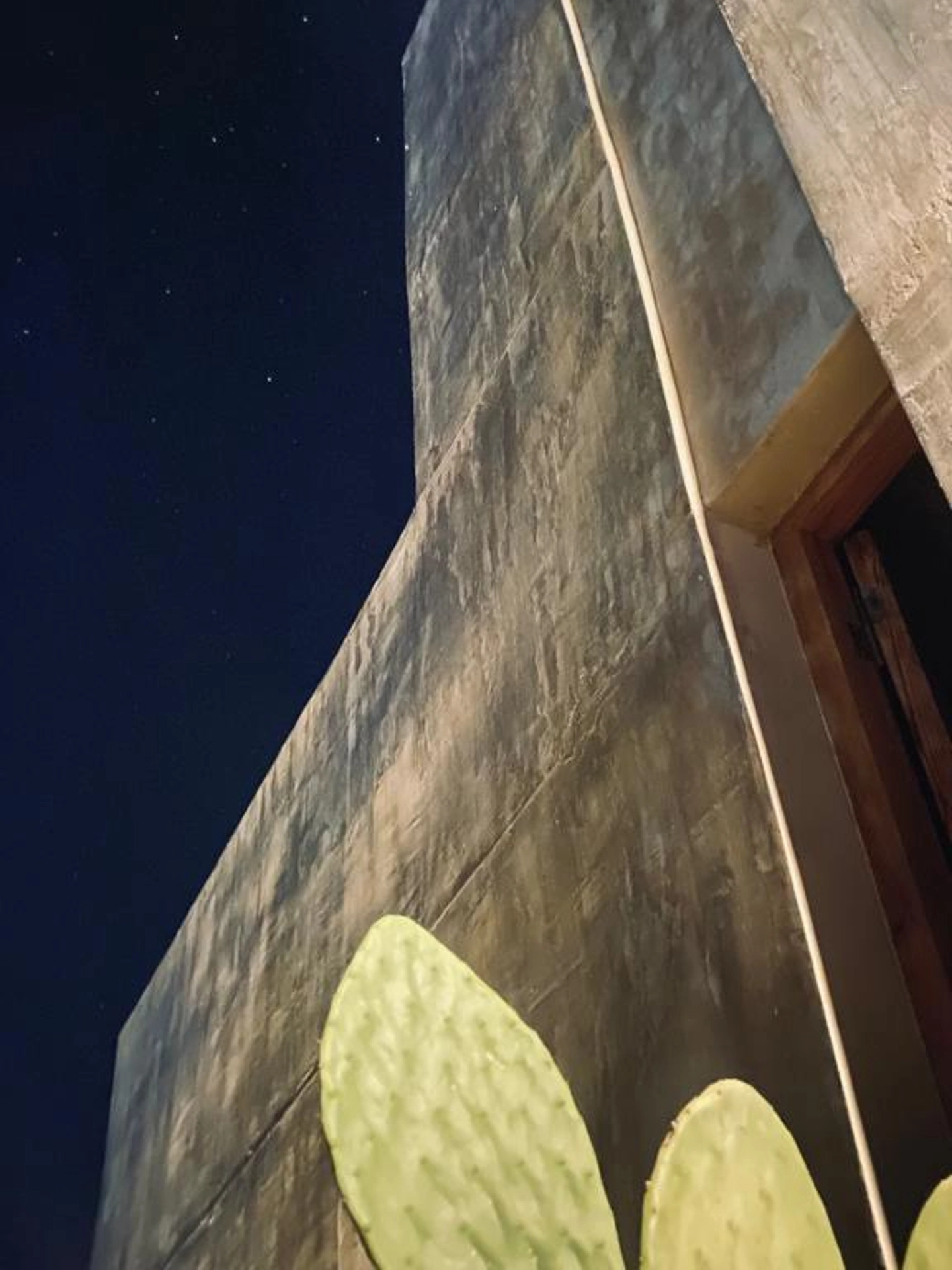 Foto de una casa en Bialet Massé construída con el sistema de Steel Framing por Vértice Construcciones en la que se observa la fachada de la casa iluminada artificialmente ya que es de noche, con un acabado símil hormigón visto en primer plano para apreciar los detalles de la terminación